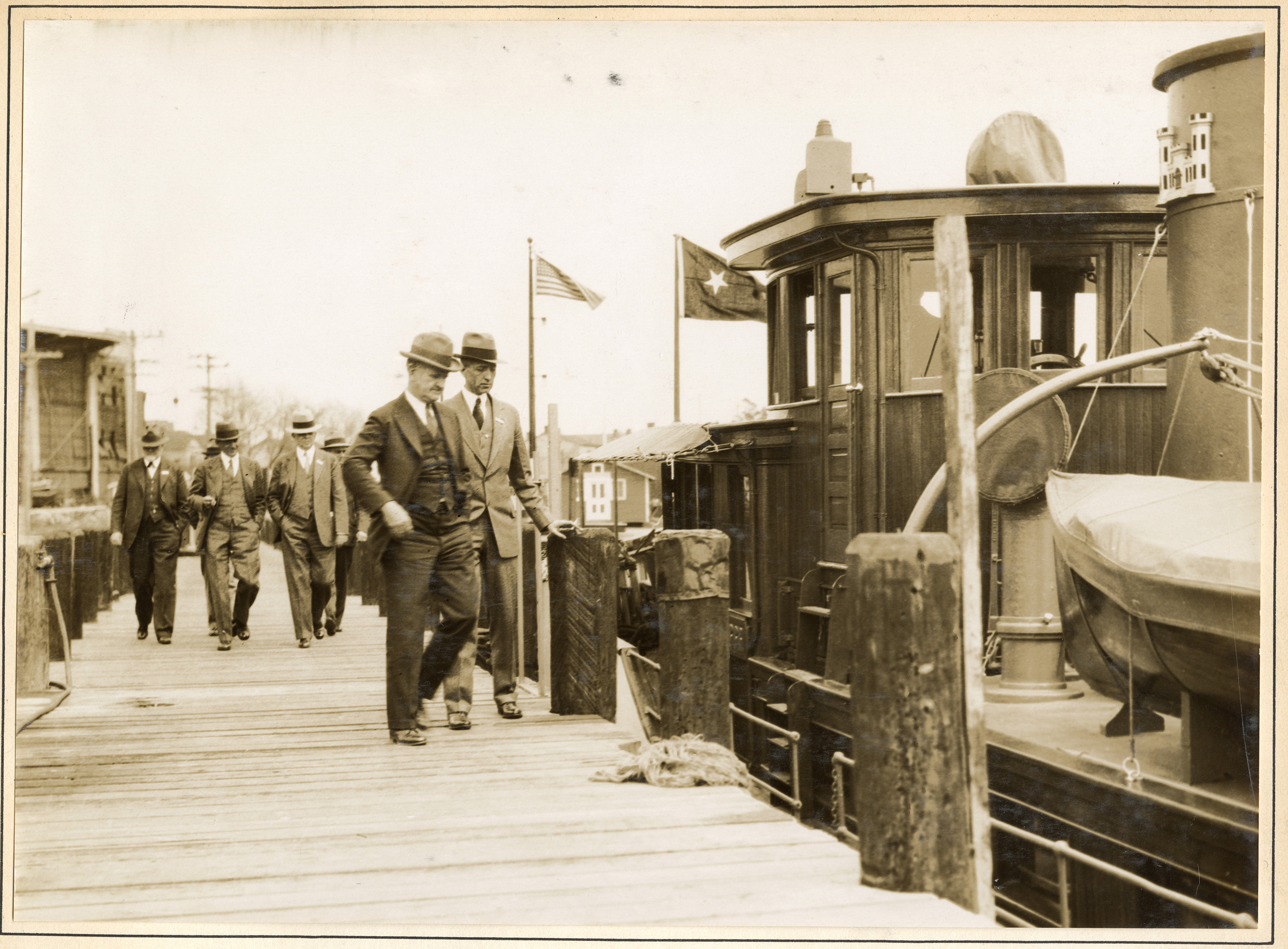 Two men in suits and hats on a dock prepare to board a small boat